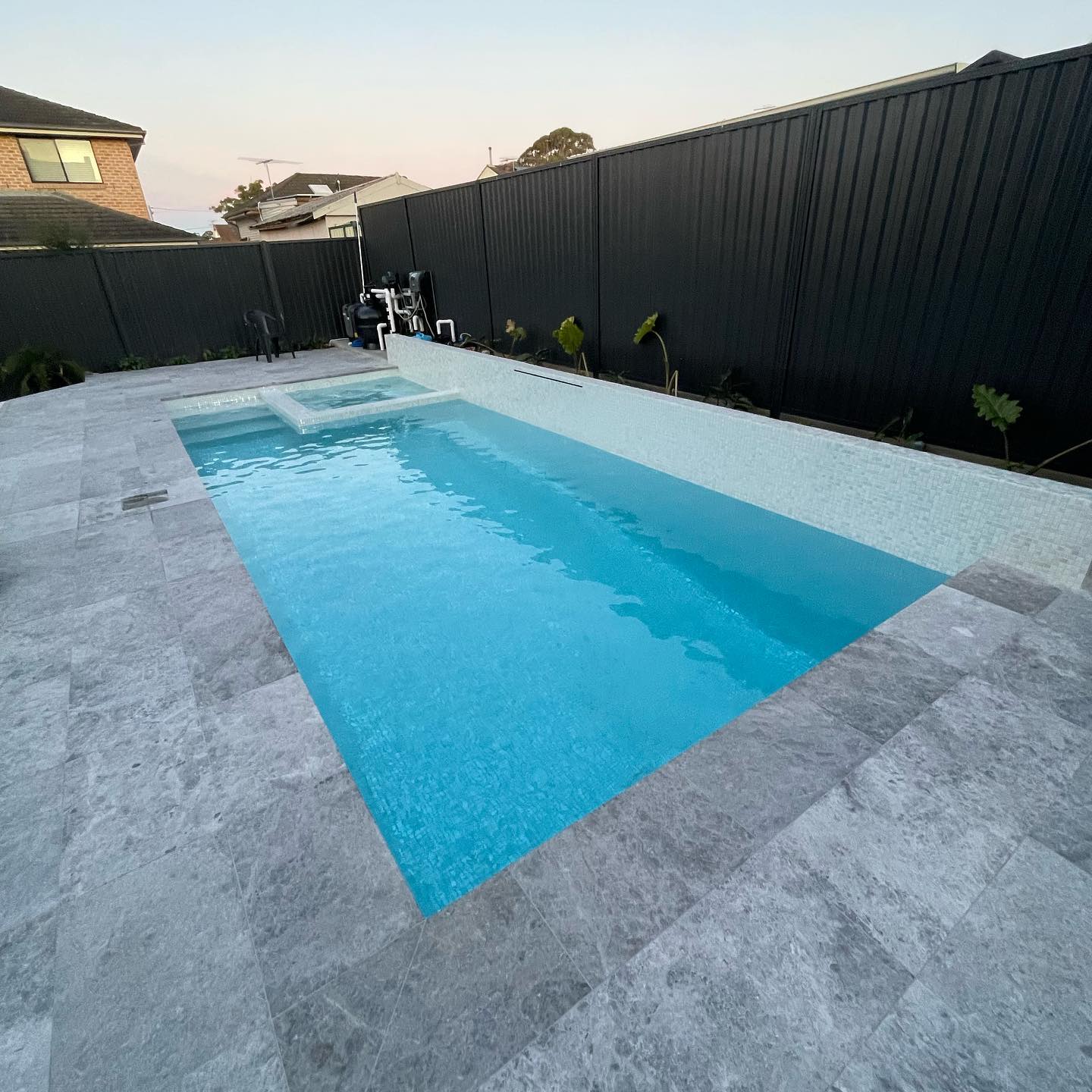 A high end residential pool with a spa and travertine coping at dusk
